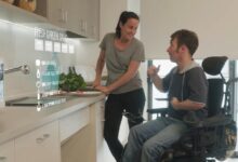 A care worker discusses meals with a person using a wheelchair in the kitchen.