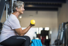 mature woman at the gym training her body and her biceps sitting in a bench with a dumbbell in her hand - healthy and fitness senior lifestyle