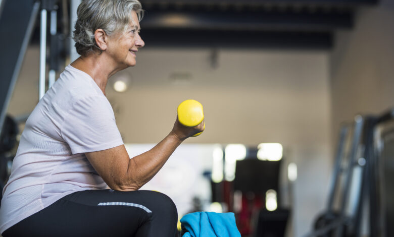 mature woman at the gym training her body and her biceps sitting in a bench with a dumbbell in her hand - healthy and fitness senior lifestyle