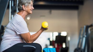 mature woman at the gym training her body and her biceps sitting in a bench with a dumbbell in her hand - healthy and fitness senior lifestyle