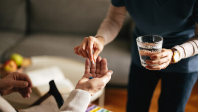 Anonymous female nurse giving pills and water to an unrecognizable senior man at the nursing home.