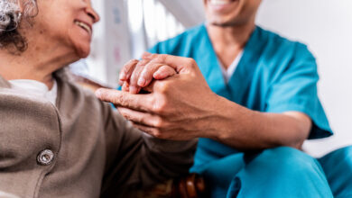 Senior woman holding caregiver's hands at home