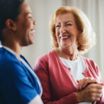 A smiling healthcare professional tends to an elderly woman, creating a moment of trust and care, showcasing a compassionate relationship in a warm and well-lit setting.