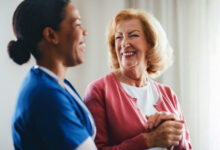 A smiling healthcare professional tends to an elderly woman, creating a moment of trust and care, showcasing a compassionate relationship in a warm and well-lit setting.