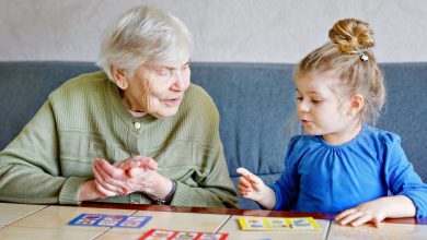 Beautiful toddler girl and grand grandmother playing together pictures lotto table cards game at home. Cute child and senior woman having fun together. Happy family indoors.