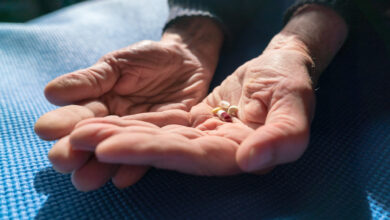 Senior hands with various pills resting on a blue mat, illuminated by warm natural sunlight