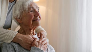 Unrecognizable female expressing care towards an elderly lady, hugging her from behind holding hands. Two adult women of different age. Family values concept. lose up, copy space, background.