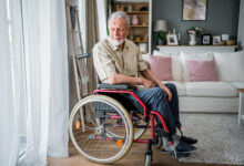 Pensive senior man in a wheelchair looking through the window at his home