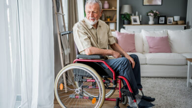 Pensive senior man in a wheelchair looking through the window at his home