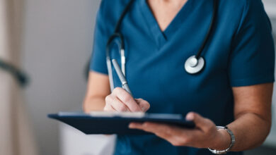 A close-up of a healthcare professional in blue scrubs writing notes on a clipboard, symbolizing care and medical professionalism in a modern medical setting.