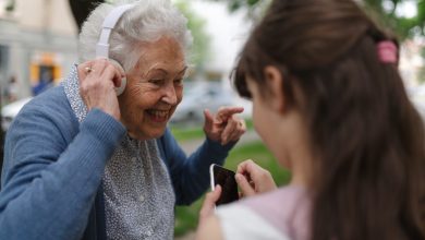 Grandma picking up young girl from school at afternoon. Granddaughter playing music on smartphone to senior grandmother with headphones.