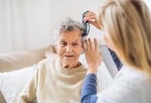 An unrecognizable health visitor combing hair of senior woman sitting on a sofa at home.