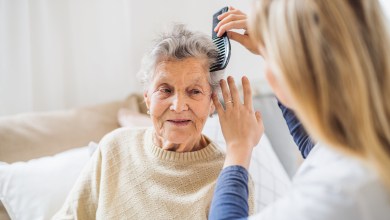 An unrecognizable health visitor combing hair of senior woman sitting on a sofa at home.