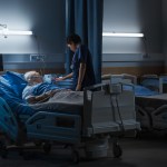 Hospital Ward: Portrait of Elderly Man Wearing Oxygen Mask Resting in Bed, Struggling to Recover after Covid-19, Sickness, Disease, Surgery. Old Man Fighting for His Life. Dark Blue Sad Shot