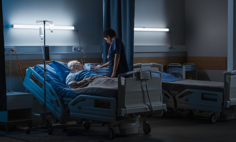 Hospital Ward: Portrait of Elderly Man Wearing Oxygen Mask Resting in Bed, Struggling to Recover after Covid-19, Sickness, Disease, Surgery. Old Man Fighting for His Life. Dark Blue Sad Shot