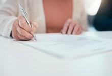 Senior hand signing finance paperwork, will agreement and pension fund contract while planning budget, banking and investing. Closeup of old, aged and retired woman calculating expenses and spending