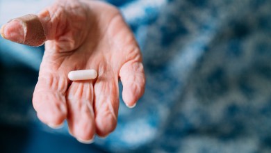 This close-up photograph features a 101 year old woman holding prescription medication pills and Vitamin Supplements in her hand. She has a bandage on her thumb. The senior adult is seated in the comfort of her domestic living room. Handling and taking pills or capsules can be difficult for individuals suffering from arthritis. The photograph captures the real-life choices and healthcare practices of this one woman as she has crossed the milestone of living beyond 100 years. The image shows the importance of medicine and healthcare in maintaining a long and healthy life.