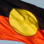The Australian Aboriginal flag flies on the Sydney Harbour Bridge. This image was taken from the foreshore of Sydney Harbour at Kirribilli on a sunny afternoon before sunset on 13 April 2024.