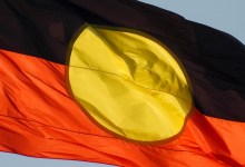 The Australian Aboriginal flag flies on the Sydney Harbour Bridge. This image was taken from the foreshore of Sydney Harbour at Kirribilli on a sunny afternoon before sunset on 13 April 2024.