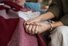 Middle aged Caucasian woman holding hand of senior Caucasian man lying under blanket, showing support and comfort, close up on hands emphasizing caregiving and compassion