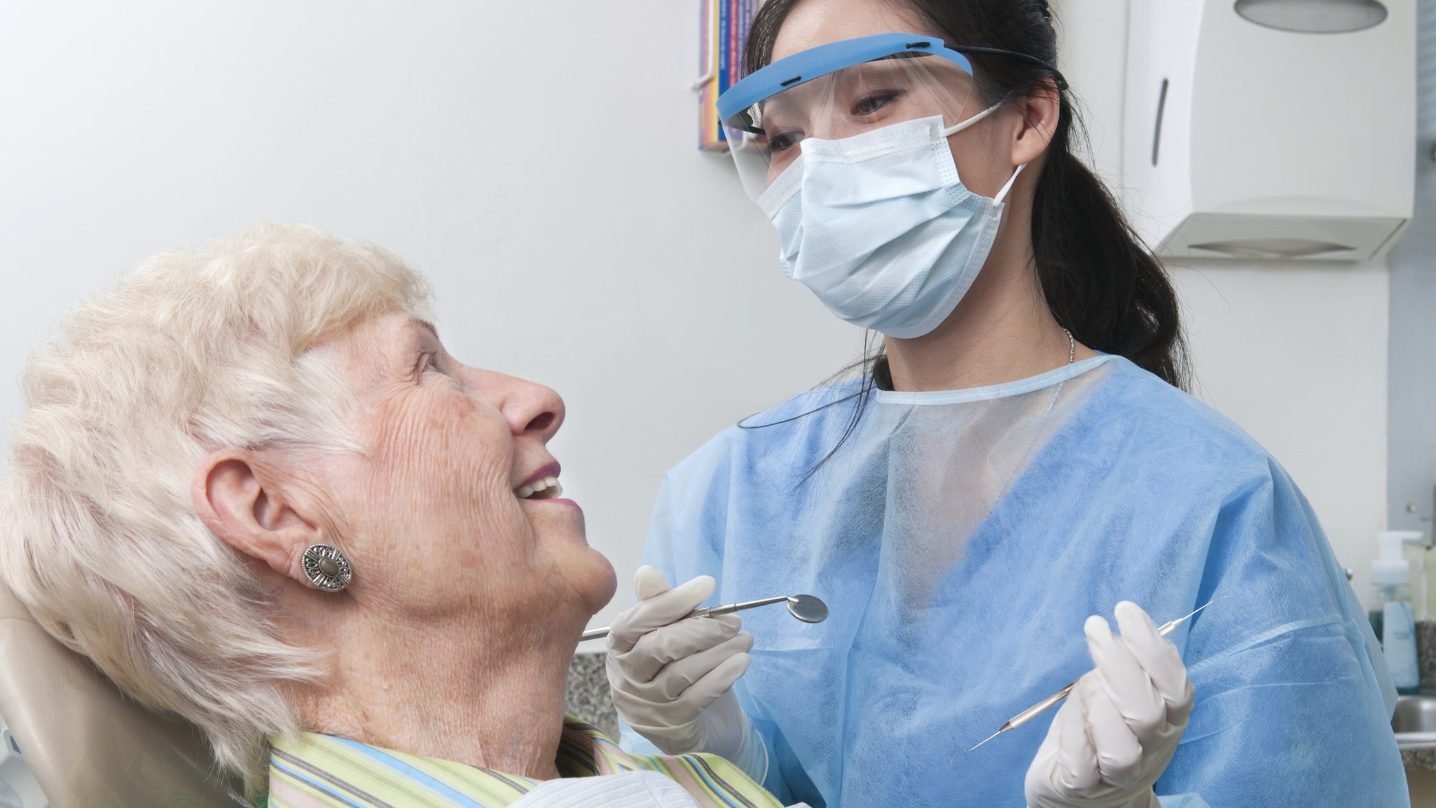 A female dental hygienist smiles and talks with an elderly female patient as she prepares to work on her teeth.