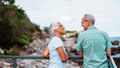 An active and adventurous multiracial senior couple cheerfully chat as they admire the ocean from a scenic coastal overlook near Portland, Maine.
