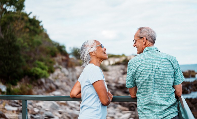 An active and adventurous multiracial senior couple cheerfully chat as they admire the ocean from a scenic coastal overlook near Portland, Maine.