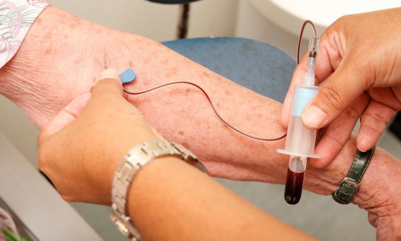 Nurse draws a vial of blood from an elderly woman for a medical test.