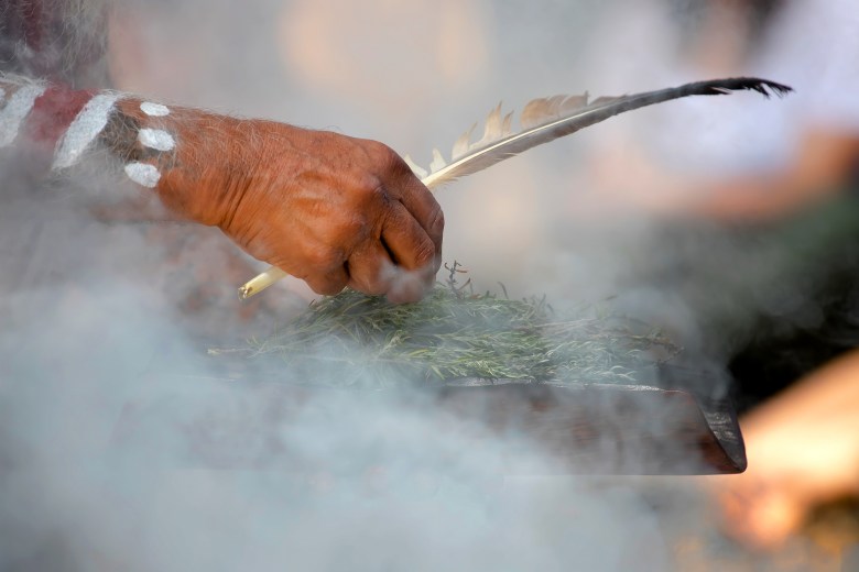 Human hand hold wooden dish and feather at the smoke ritual rite at a indigenous community event in Australia