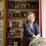 Senior woman wearing glasses lost in thought while looking out through a window in her living room at home