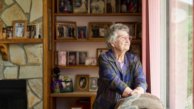 Senior woman wearing glasses lost in thought while looking out through a window in her living room at home