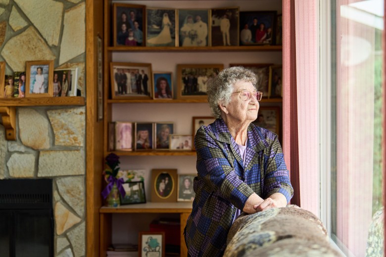 Senior woman wearing glasses lost in thought while looking out through a window in her living room at home