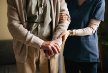 An anonymous Japanese female caregiver supporting elderly patient to stand and walk with a walking cane at the nursing home.