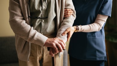 An anonymous Japanese female caregiver supporting elderly patient to stand and walk with a walking cane at the nursing home.