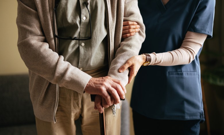An anonymous Japanese female caregiver supporting elderly patient to stand and walk with a walking cane at the nursing home.