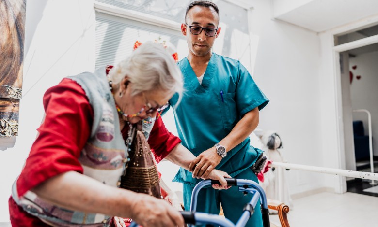 Caregiver helping senior woman walk with walker at nursing home