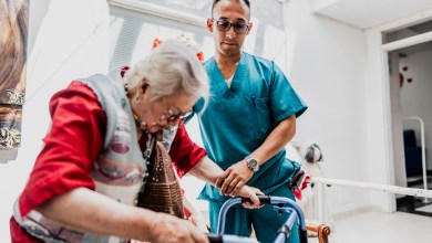 Caregiver helping senior woman walk with walker at nursing home