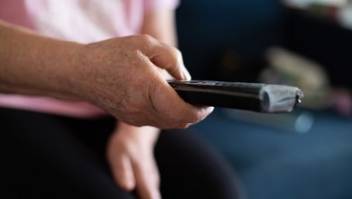 elderly senior woman with remote controller in hands sitting on sofa in living room at home and switching channels watching TV enjoying home leisure in retirement.