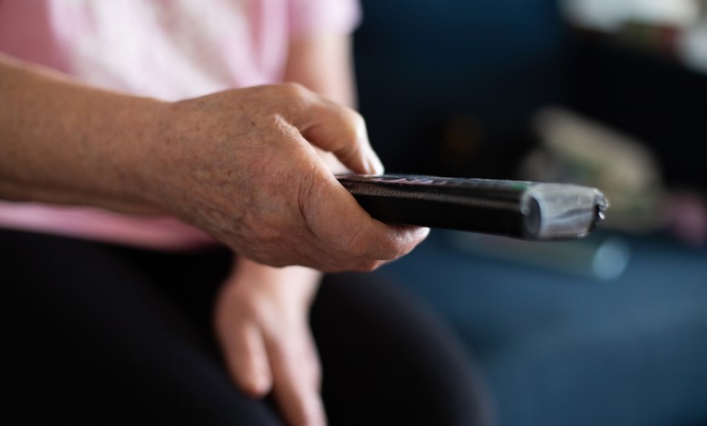 elderly senior woman with remote controller in hands sitting on sofa in living room at home and switching channels watching TV enjoying home leisure in retirement.